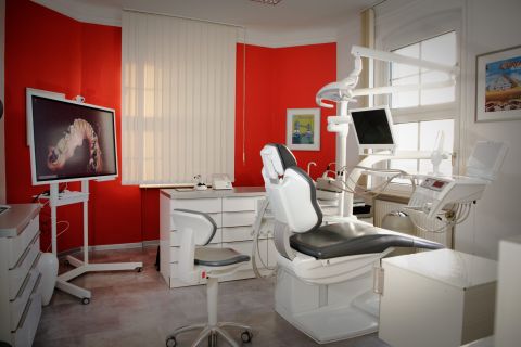 Behandlungszimmer mit Behandlungsstuhl, Bildschirm und roter Wand