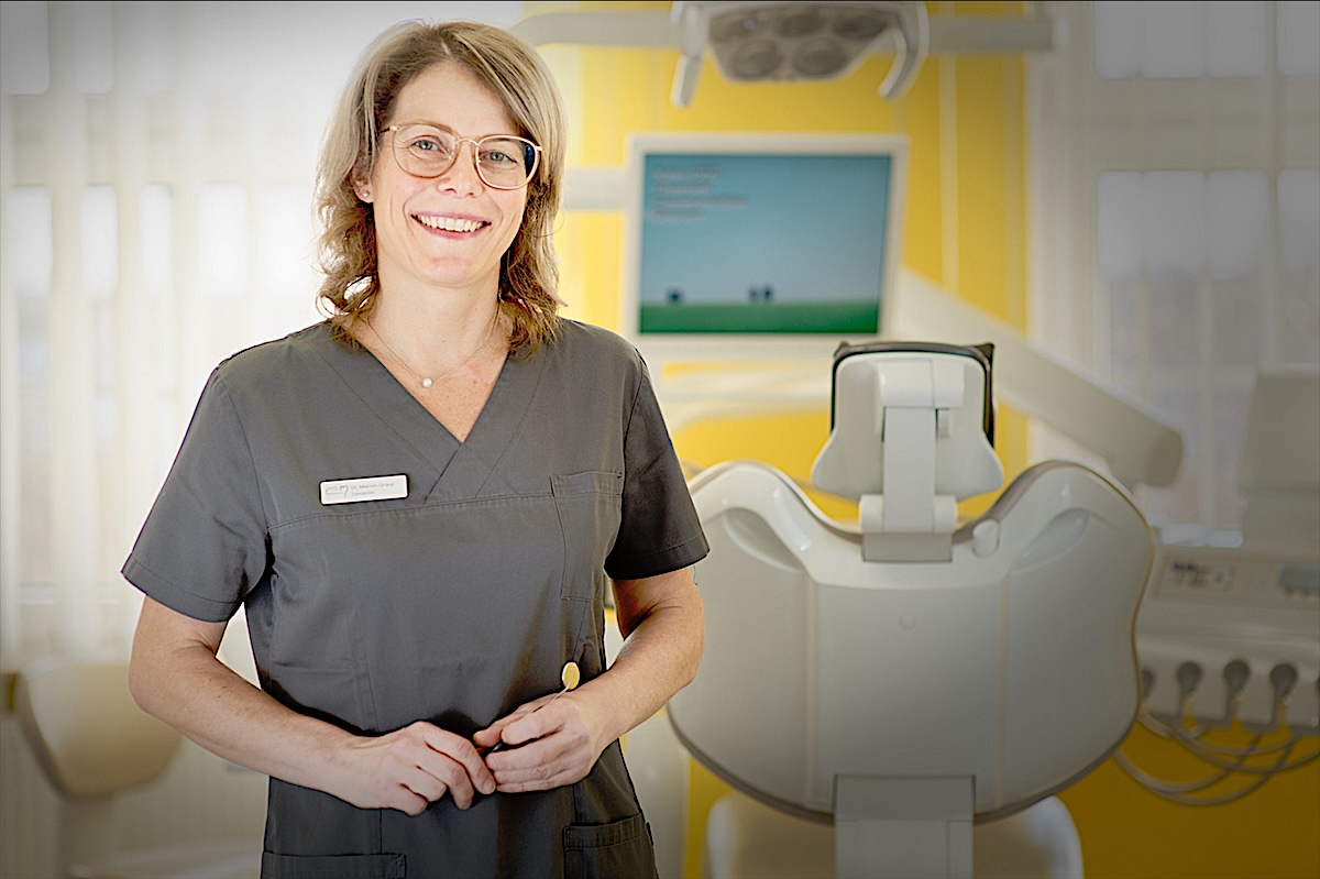 Dr. Marion Graup lächelnd in grauer Praxiskleidung im Behandlungszimmer